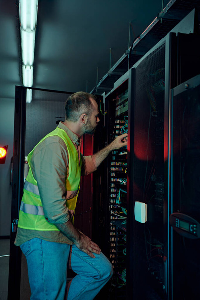 handsome technician with beard in safety vest inspecting data center attentively, maintenance - Photo, Image