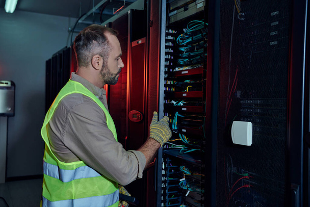 good looking professional in safety gloves and vest inspecting information storage, data center - Photo, Image