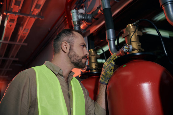 bon technicien concentré dans les vêtements de sécurité vérifier les bouteilles de gaz pendant le travail, centre de données - Photo, image