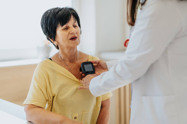 Een huisarts onderzoekt een oudere vrouw zorgvuldig met een stethoscoop en controleert haar bloeddruk. Er vindt een professionele raadpleging plaats, waarbij gezondheidsproblemen en behandelingsmogelijkheden worden besproken.. - Foto, afbeelding
