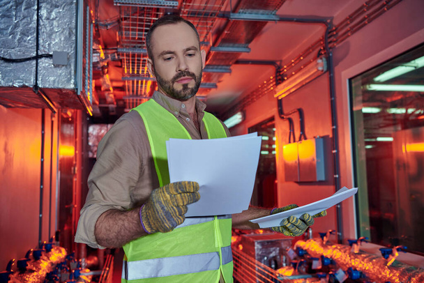 focused hardworking specialist in safety clothes looking attentively at his paperwork, data center - Photo, Image