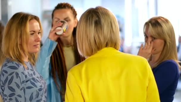 cztery kobiety w biurze podczas przerwy komunikują się piją herbatę plotki śmieją się żółte niebieskie ubrania świętują firmowe blondynki. jeden z czerwonymi dredami na jej złamanej głowie - Materiał filmowy, wideo