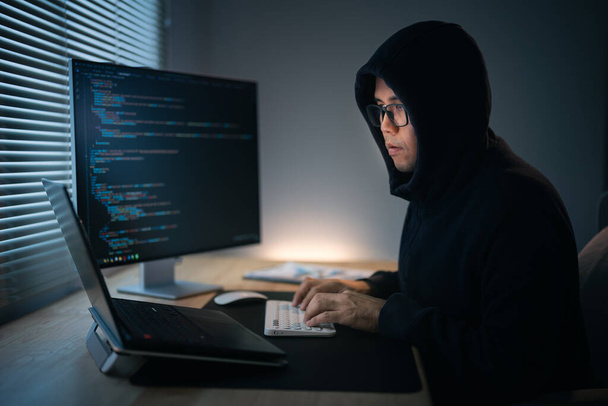 ハッカーの男は,ネットワークセキュリティシステムをハッキングするためにフードライティングコードを身に着けています. 危険なフード付きハッカーが政府のデータサーバーに侵入し,そのシステムにウイルスが感染します. ハッキングとマルウェアの概念. - 写真・画像
