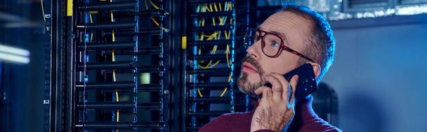concentrated professional in turtleneck with glasses and beard talking by phone, data center - Photo, Image