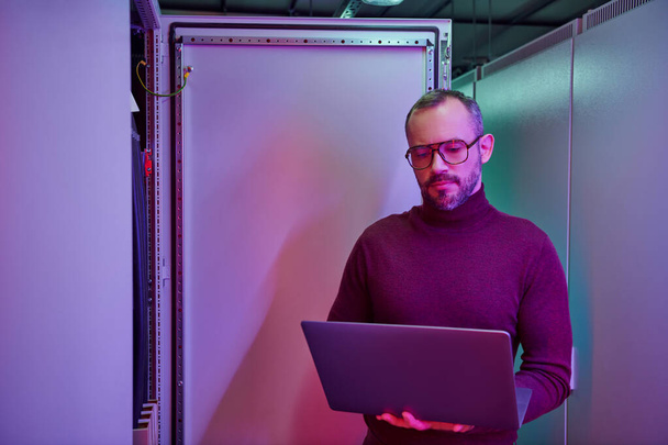 handsome hardworking data center specialist in turtleneck looking at his laptop attentively - Photo, Image