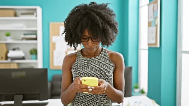 Afroamerikanerin lächelt selbstbewusst mit Smartphone im Büro - Filmmaterial, Video