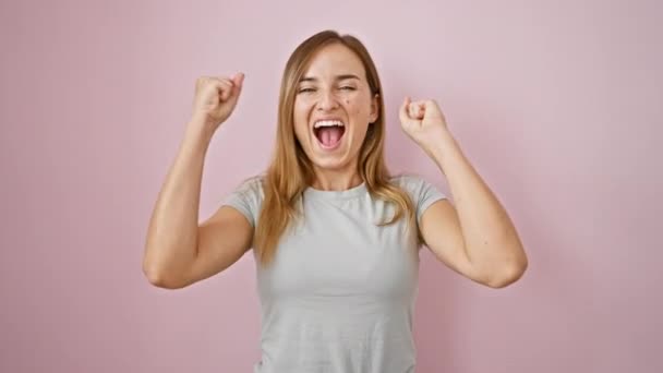 Selbstbewusste junge blonde Frau feiert mit einem freudigen Lächeln vor isoliertem rosa Hintergrund - Filmmaterial, Video
