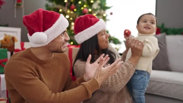 Pareja e hijo sosteniendo la bola de decoración sentados en el suelo por el árbol de Navidad en casa - Imágenes, Vídeo