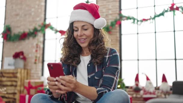 Mujer hispana de mediana edad usando teléfono inteligente celebrando la Navidad en casa - Metraje, vídeo
