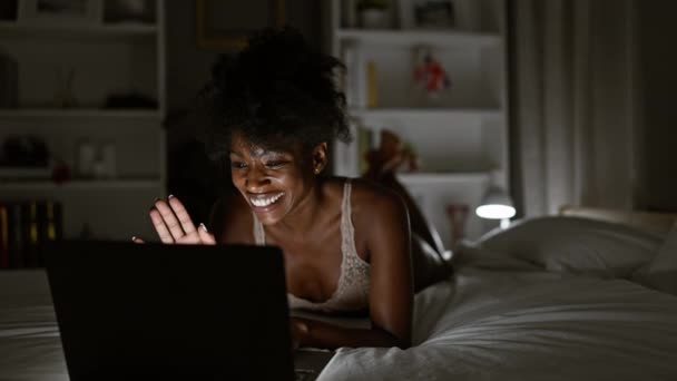 Αφροαμερικανή γυναίκα που φοράει εσώρουχα με βιντεοκλήση ξαπλωμένη στο κρεβάτι στο υπνοδωμάτιο - Πλάνα, βίντεο