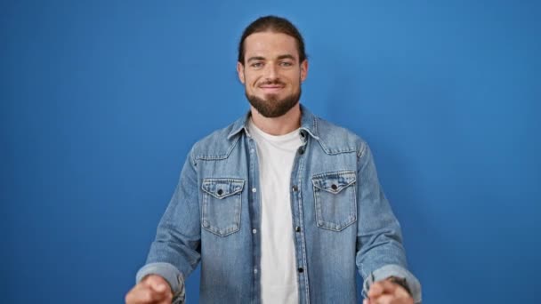 Joven hombre hispano sonriendo confiado haciendo gesto del dedo medio sobre fondo azul aislado - Metraje, vídeo