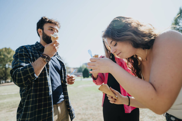 Young, carefree friends spend a sunny day in the park, laughing, eating ice cream, and socializing. They embrace the freedom and well-being that comes with enjoying nature together. - Photo, Image