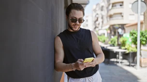 Jonge Spaanse man draagt een zonnebril met smartphone op straat - Video