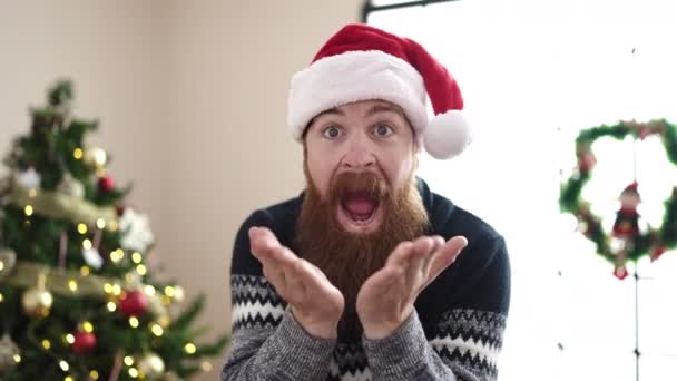 Young redhead man standing by christmas tree kissing at home - Footage, Video