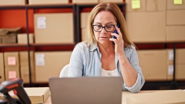 Mujer hispana de mediana edad comercio electrónico trabajador de negocios utilizando portátil hablando en el teléfono inteligente en la oficina - Imágenes, Vídeo