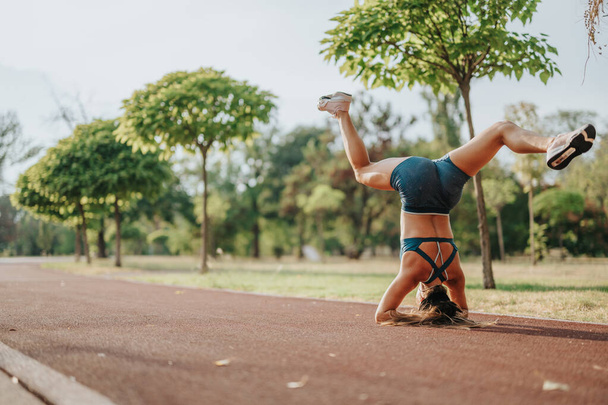 Een atletisch meisje toont haar kracht en flexibiliteit in een groen park. Met balans en gratie, ze voert een headstand pose, inspireren van een gezonde levensstijl. - Foto, afbeelding