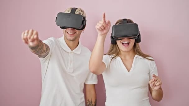 Όμορφο ζευγάρι παίζει βιντεοπαιχνίδι χρησιμοποιώντας γυαλιά εικονικής πραγματικότητας πάνω από απομονωμένο ροζ φόντο - Πλάνα, βίντεο