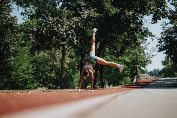 Una mujer activa y en forma practica volteretas en un parque soleado. Su ropa deportiva y músculos muestran su dedicación al entrenamiento al aire libre. - Foto, imagen