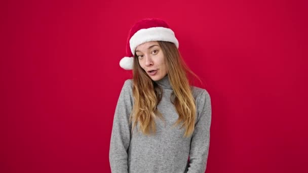 jonge Kaukasische vrouw glimlachen zelfverzekerd dragen kerst hoed over geïsoleerde rode achtergrond - Video