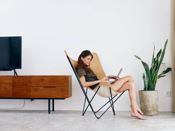 Γυναικεία σπουδαστική μελέτη κάθεται σε μια καρέκλα με ένα φορητό υπολογιστή εργασίας στο σπίτι χαμόγελο, μοντέρνο κομψό εσωτερικό σκανδιναβικό τρόπο ζωής, αντίγραφο χώρου. Υψηλής ποιότητας φωτογραφία - Φωτογραφία, εικόνα