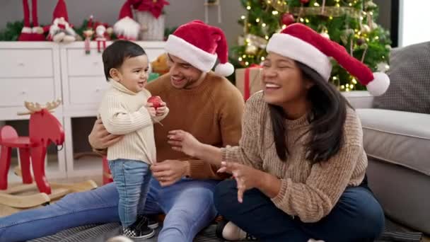 Ζευγάρι και γιος κάθονται στο πάτωμα δίπλα στο χριστουγεννιάτικο δέντρο παίζοντας στο σπίτι - Πλάνα, βίντεο
