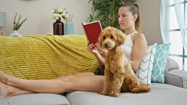 Evde kanepede oturan köpek okuma kitabı olan beyaz bir kadın. - Video, Çekim