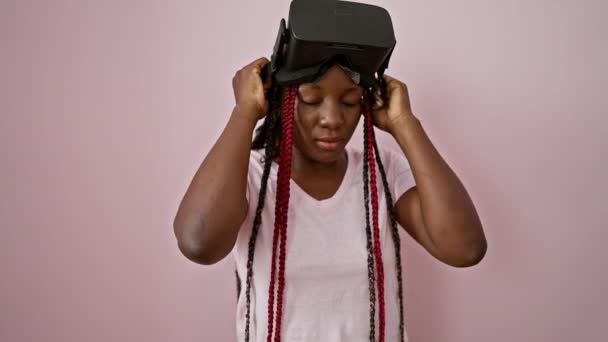 Jolly african american γυναίκα gaming μακριά, στέκεται με σιγουριά πάνω από το ροζ απομονωμένο φόντο, παίζοντας βιντεοπαιχνίδι με γυαλιά εικονικής πραγματικότητας - Πλάνα, βίντεο