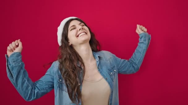 Junge schöne hispanische Frau lächelt selbstbewusst und trägt Weihnachtsmütze, die über isoliertem rotem Hintergrund tanzt - Filmmaterial, Video