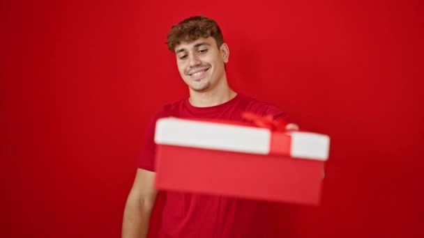 Cheerful young hispanic guy casually pointing at camera over isolated red background, confidently holding birthday gift, his handsome smile expressing pure joy and positive lifestyle. - Footage, Video