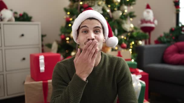 Giovane uomo ispanico seduto sul pavimento da albero di Natale baciare a casa - Filmati, video