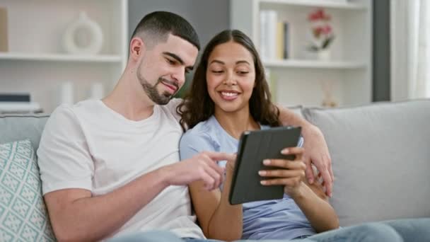 Усміхнена красива пара насолоджується технологіями разом вдома, випадковим способом життя впевненого чоловіка і жінки, сидячи на дивані, використовуючи тачпад - Кадри, відео