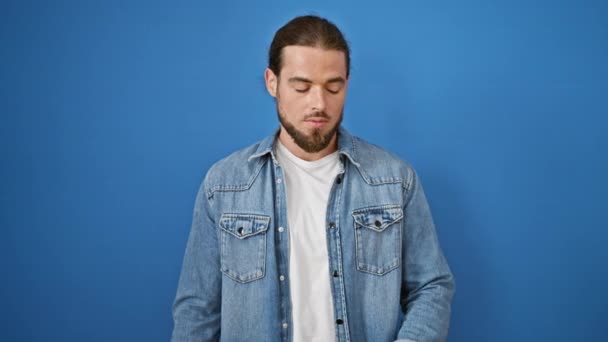 Jonge Spaanse man op zoek horloge met nerveuze uitdrukking over geïsoleerde blauwe achtergrond - Video