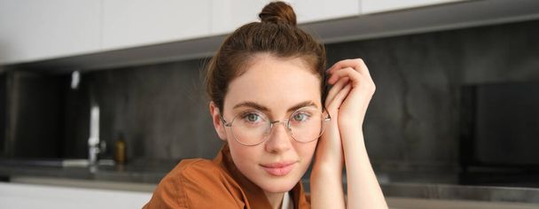 Крупним планом портрет брюнетки в окулярах, красива жіноча модель сидить на кухні, сміється і посміхається, експресує безтурботні, позитивні емоції. - Фото, зображення