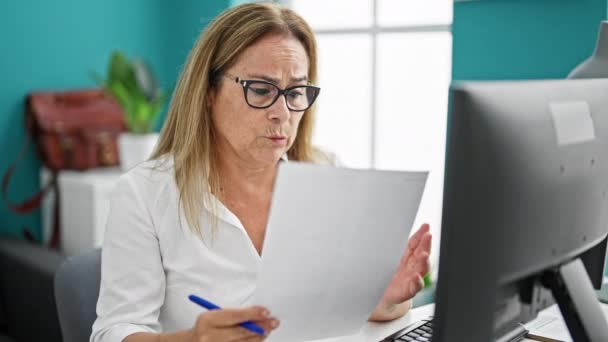 Lavoratrice ispanica di mezza età che utilizza il documento di lettura del computer in ufficio - Filmati, video