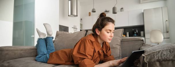 Weekend en lifestyle concept. Jonge vrouw liggend op de bank met digitale tablet, scrollen sociale media, e-book lezen of tv-series kijken op app. - Foto, afbeelding
