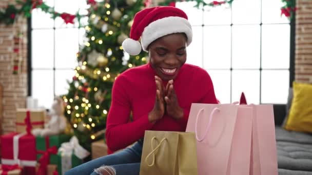 Mujer afroamericana celebrando la Navidad buscando bolsas de compras en casa - Imágenes, Vídeo