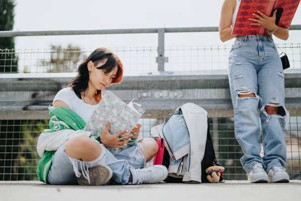 Két középiskolás egy városi városban ül a szabadban, és együtt tanulnak egy vizsgára. Együttműködésük és barátságuk hozzájárul jobb jegyeikhez és tanulságaikhoz.. - Fotó, kép