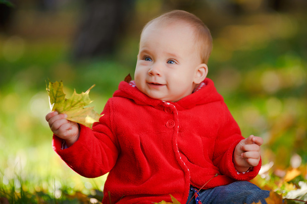 Cheerful baby in a red dress playing with yellow leaves - Foto, afbeelding