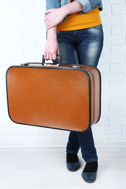 Woman holding old suitcase on brick wall background - Foto, imagen