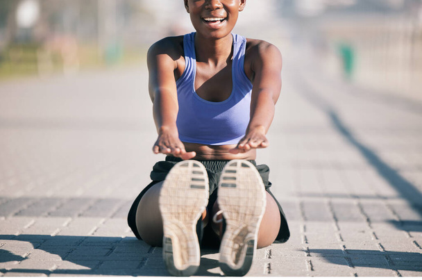 Exercise, happy woman and stretching legs to touch feet for fitness, training or performance on urban ground. Female athlete, smile and warm up for flexible workout, muscle mobility and sports in sun. - Photo, Image