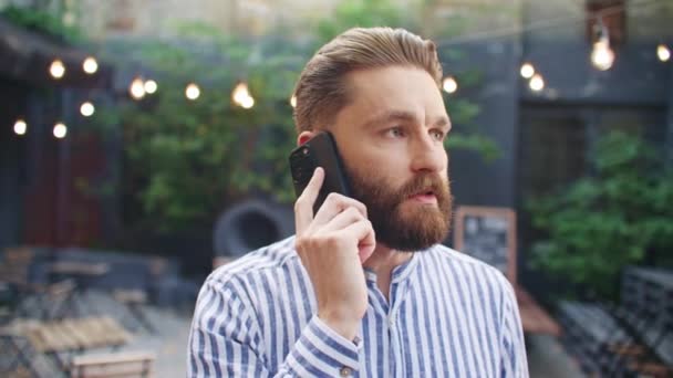 Kafe terasının yanında duran yakışıklı beyaz adam telefonuyla konuşuyor. Genç erkek girişimci ortağıyla uzaktan kumandayla konuşuyor. Cidden yeni bir bar açmaktan mı bahsediyorsun?. - Video, Çekim