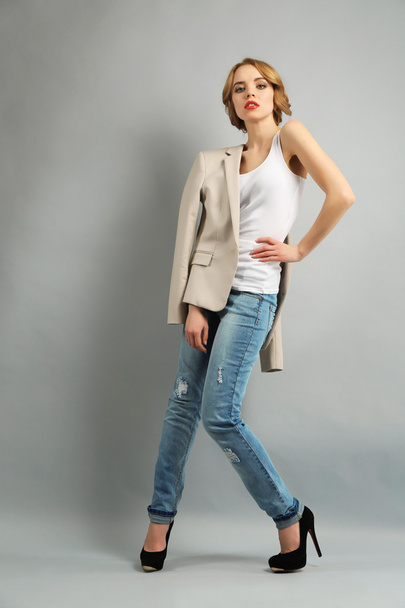 Beautiful young woman in jacket and jeans posing on light background - Photo, image