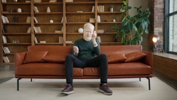 El tipo Albino tocando tambores invisibles divirtiéndose en el sofá en el apartamento loft. Entretenimiento estilo de vida, música y jóvenes felices concepto. Hombre extático soñando. Emocionado baterista entrenamiento músico en casa - Imágenes, Vídeo
