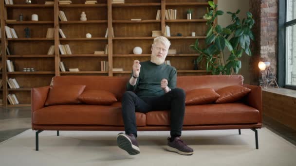 Emocionado hombre albino hipster tocando tambores invisibles que se divierten en el sofá en el apartamento de estilo loft moderno. Entretenimiento estilo de vida, música y jóvenes felices concepto. extático macho profundo en su sueños 4K - Metraje, vídeo