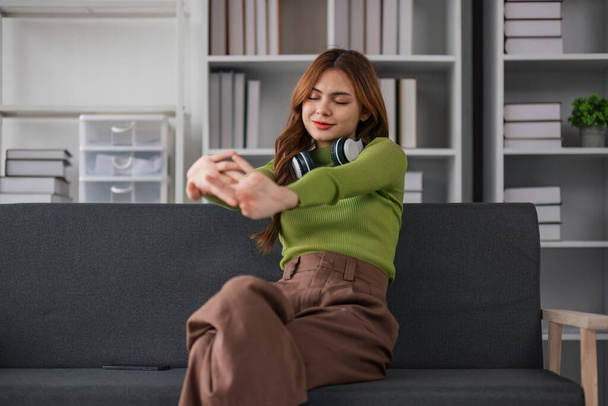 Ασιάτισσα γυναίκα που ακούει μουσική ενώ κάθεται στον καναπέ Ελκυστική νεαρή γυναίκα που φοράει ακουστικά αισθάνεται ευτυχισμένη περνώντας ελεύθερο χρόνο στο σπίτι και απολαμβάνοντας τις δραστηριότητες του Σαββατοκύριακου στο σπίτι.. - Φωτογραφία, εικόνα