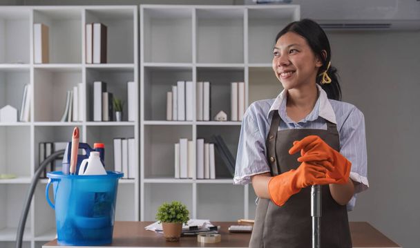 Retrato de uma bela jovem dona de casa sorrindo e feliz, segurando suprimentos de limpeza no escritório. material de limpeza, governanta. - Foto, Imagem