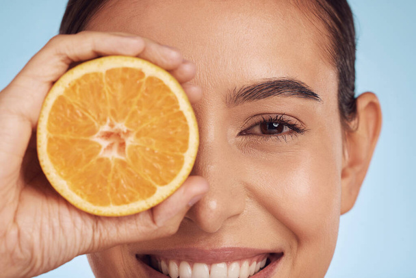 Closeup woman, portrait and orange for vitamin C, diet or skincare against a blue studio background. Face of happy person smile with organic citrus fruit in natural nutrition, spa or facial treatment. - Photo, Image