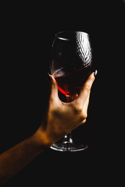Ένα ποτήρι κόκκινο κρασί στα χέρια μιας σέξι γυναίκας με κόκκινο φόρεμα. - Φωτογραφία, εικόνα