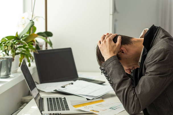 Zdjęcie portretu zmęczonego faceta z bólem głowy trzymającego most nosa palcami przy stole w nowoczesnym biurze przemysłowym w pomieszczeniach. Wysokiej jakości zdjęcie - Zdjęcie, obraz