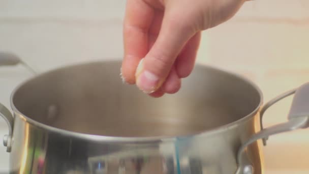 Plan rapproché de la main du cuisinier mâle ajoutant du sel à l'eau bouillante dans une casserole en métal. Concentration sélective - Séquence, vidéo